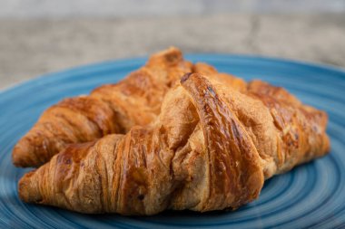 Mavi yuvarlak bir tabağa yerleştirilmiş lezzetli tereyağlı kruvasanlar. Yüksek kalite fotoğraf
