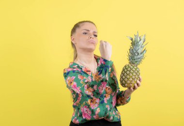 Taze ananaslı genç bir kadın sarı duvara poz veriyor. Yüksek kalite fotoğraf