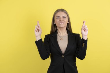 Çekici bir iş kadınının sarı duvarda gülümseyen ve parmaklarını çapraz gösteren bir resmi. Yüksek kalite fotoğraf