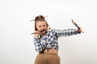 Beyaz bir duvarın üzerinde fırça tutan ve poz veren genç bir sanatçının portresi. Yüksek kalite fotoğraf