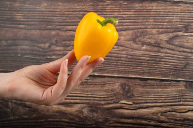 Ahşap arka planda sarı dolma biber tutan kadın eli. Yüksek kalite fotoğraf