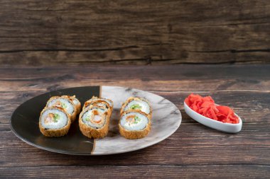 Ahşap yüzeyde mermer bir tabak lezzetli tempura rulo ve zencefil turşusu. Yüksek kalite fotoğraf