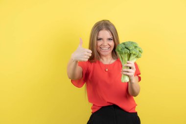 Büyük yeşil brokolisi olan güzel bir kadın modelin başparmağı görünüyor. Yüksek kalite fotoğraf