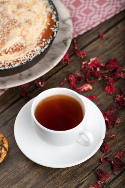 Hindistan cevizi parçalı bir tabak tatlı turta, gül yaprakları ve ahşap arka planda bir fincan çay. Yüksek kalite fotoğraf