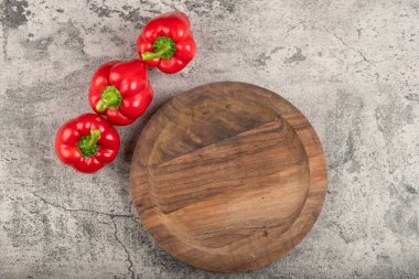 Wooden plate and ripe red bell peppers on stone surface. High quality photo