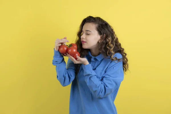 Młoda Nastolatka Niebieskiej Bluzie Pachnie Czerwonymi Pomidorami Stoi Żółtym Tle — Zdjęcie stockowe