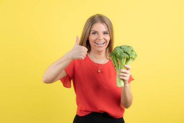 Büyük yeşil brokolisi olan güzel bir kadın modelin başparmağı görünüyor. Yüksek kalite fotoğraf