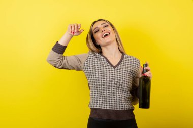 Sarı arka planda bira şişesi olan genç ve güzel bir kadın.