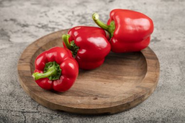 Wooden plate of ripe red bell peppers on stone surface. High quality photo