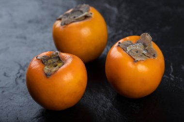 Siyah yüzeye yerleştirilmiş üç taze fuyu hurması. Yüksek kalite fotoğraf