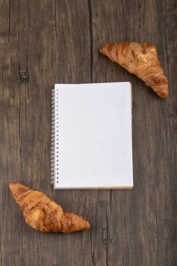 Tahta masaya beyaz defter konmuş lezzetli tereyağlı kruvasanlar. Yüksek kalite fotoğraf