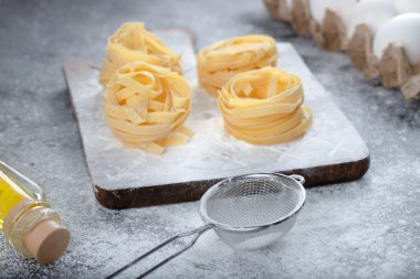 Çiğ tagliatelle, siyah yüzeyde un, yağ ve çiğ yumurta ile yuva yapar. Yüksek kalite fotoğraf