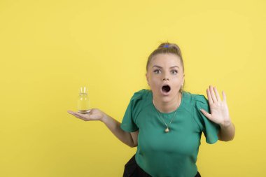 Gayri resmi kıyafetli güzel bir kadın sarı arka planda bir bardak su tutuyor. Yüksek kalite fotoğraf