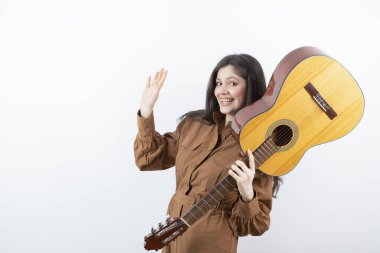 Beyaz duvarda gitar tutan esmer bir kadın modeli. Yüksek kalite fotoğraf