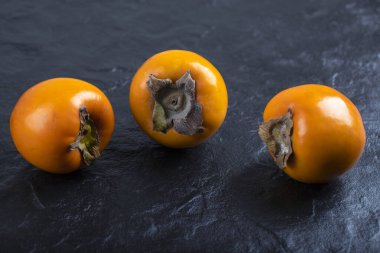 Siyah yüzeye yerleştirilmiş üç taze fuyu hurması. Yüksek kalite fotoğraf