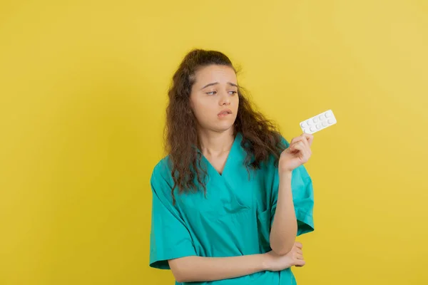 Jovem Enfermeira Uniforme Olhando Para Pílulas Médicas Sobre Parede Amarela — Fotografia de Stock