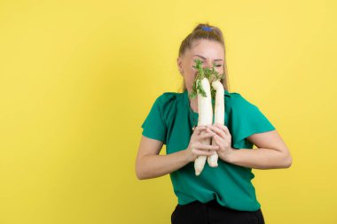 Sarışın turp tutan ve sarı duvarın üzerinde duran güzel bir kadın. Yüksek kalite fotoğraf