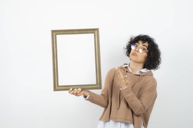 Kıvırcık esmer kadın boş resim çerçevesiyle poz veriyor.
