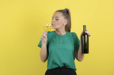 Genç ve güzel bir kadın sarı arka planda bir bardak şarap içiyor. Yüksek kalite fotoğraf