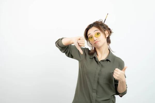 Portrait of girl with messy bun in glasses standing and giving thumbs up. High quality photo