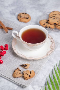 Bir fincan çay ve kuru üzümlü ve tarçınlı kurabiyeler. Gri arka planda çubuklar, yakın görüş.
