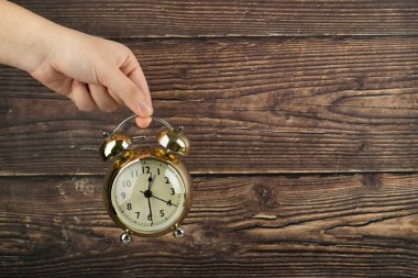 Female hand holding alarm clock on wooden background. High quality photo