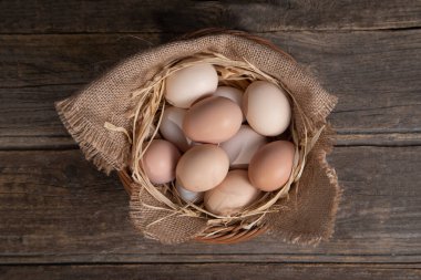 Tahta bir arka planda hasır sepetteki tavuk yumurtaları.