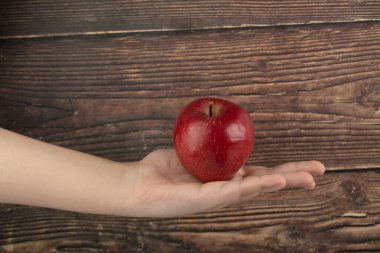 Erkek el, tahta arka planda taze kırmızı elmayı tutuyor. Yüksek kalite fotoğraf