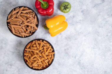 Mermer arka planda pişmemiş Penne rigate ve fusilli makarna dolu kaseler. Yüksek kalite fotoğraf