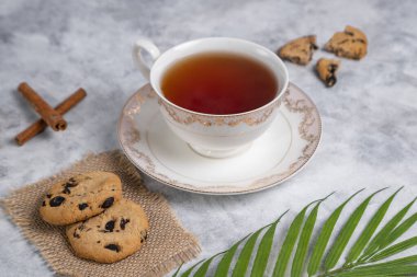 Bir fincan çay ve kuru üzümlü ve tarçınlı kurabiyeler. Gri arka planda çubuklar, yakın görüş.