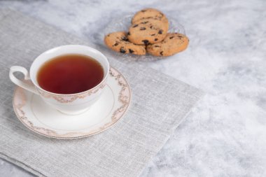 Bir fincan çay ve kuru üzümlü ve tarçınlı kurabiyeler. Gri arka planda çubuklar, yakın görüş.