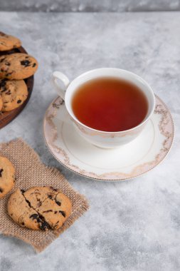 Bir fincan çay ve kuru üzümlü ve tarçınlı kurabiyeler. Gri arka planda çubuklar, yakın görüş.