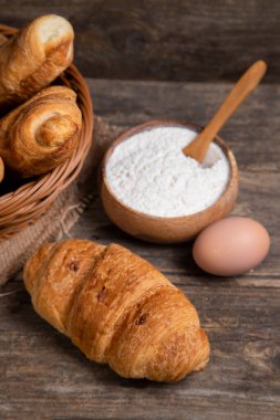 Taze pişmiş kruvasan, kahverengi tavuk yumurtası ve un ile ahşap bir masa. Yüksek kalite fotoğraf