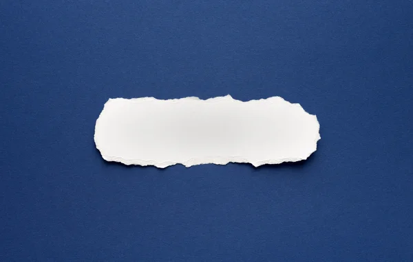 Un trozo de papel roto sobre un fondo azul — Foto de Stock