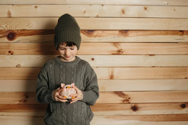 Retrato de lindo niño sonriente con alcancía sobre fondo de madera. Niño con dinero en sombrero verde. —  Fotos de Stock