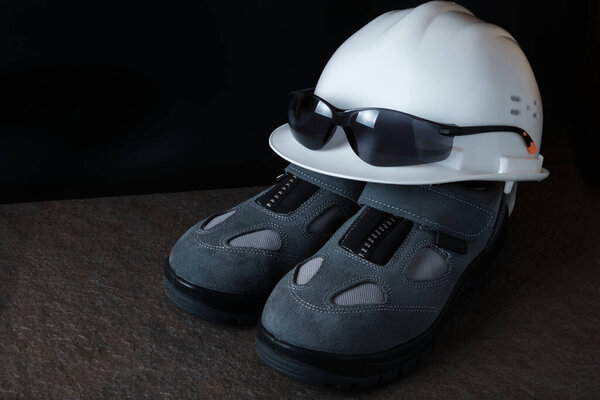 Hardhat, protective eyewear and pair of new protective shoes on stone floor. Industrial safety equipment for workers.