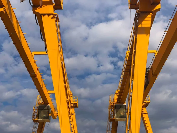 Gantry cranes opposite cloudy sky. Industrial lifting machinery. Hoist, winch