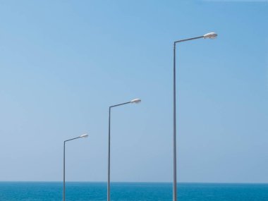 Deniz ve mavi gökyüzünün karşısındaki üç ışık direği. Kopyalama alanı olan minimalist manzara