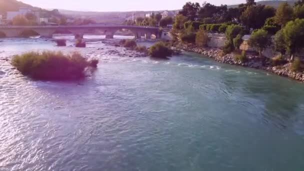 Wide mountain river with rapid at shallow and old roman bridge in the sunset — Stok Video