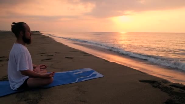 Mann sitzt in Lotusposition am Strand — Stockvideo