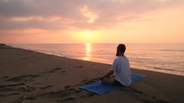 Adam sahilde lotus pozisyonunda oturuyor.