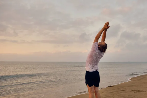Человек практикует Сурья Намаскар позировать на морском пляже — стоковое фото