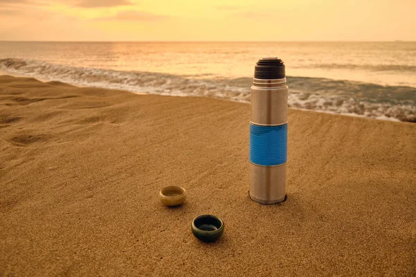 Vacuum flask and tea cups on a sandy beach