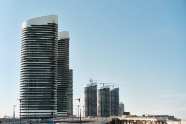 Açık mavi gökyüzüne karşı yükselen uzun ve modern gökdelenler, bazı binalar hala yapım aşamasında. Çağdaş şehir manzarasının gelişimi ve dönüşümü. Yeni Alamein, Matrouh Valiliği, Mısır