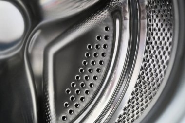 Modern bir ev aletinin yapısını gösteren delinmiş desenli ve cilalı yüzeyi olan metalik bir çamaşır makinesi varilinin ayrıntılı yakın plan görüntüsü.