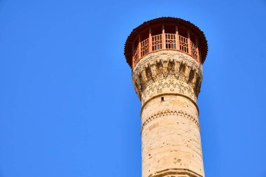 Açık mavi gökyüzüne karşı yükselen süslü tarihi minarenin alçak açılı görüntüsü. Geleneksel İslami mimari, detaylı taş işçiliği, kültürel miras, din, mimari tarih. Gaziantep, Türkiye