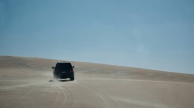Tek bir off-road aracı açık mavi gökyüzünün altında engin kumlu çöl tepelerini aşıyor. Macera, keşif ve aşırı kurak bir ortamda seyahat. Siwa vahası yakınlarındaki Batı Çölü, Mısır