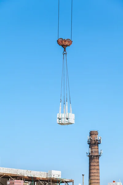heavy load hanging on the hook of a crane under construction and the construction of a brick chimney boile
