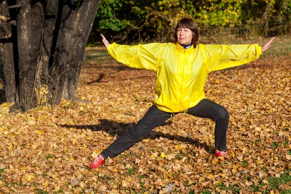 Elderly pretty woman doing exercise in autumn forest glade