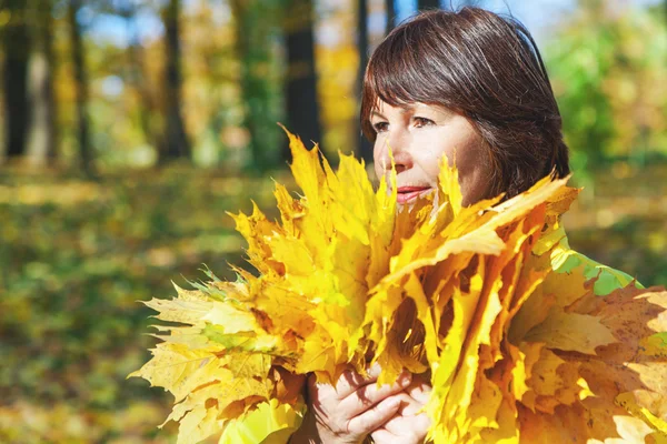 Düşmüş bir akçaağaç yaprakları tutan sevimli yaşlı kahverengi saçlı